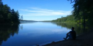 Person by a tranquil lake, reflecting on life.